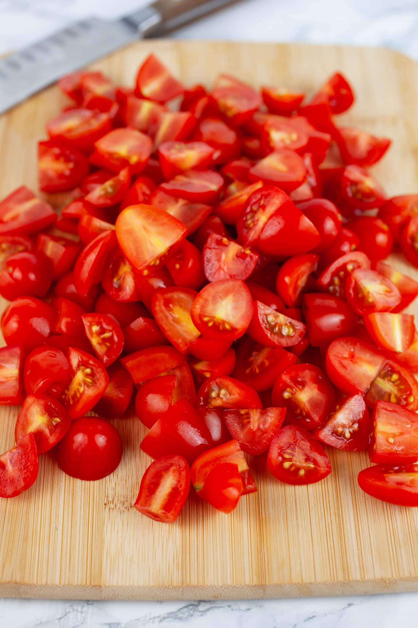 Chopped grape tomatoes on wooden cutting board with knife.