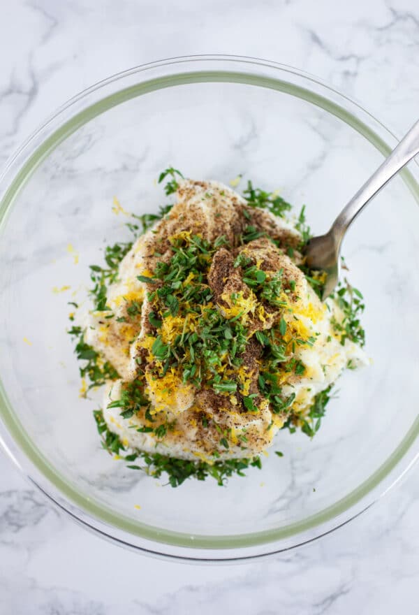 Ricotta cheese with lemon zest and minced herbs in small glass bowl with fork.