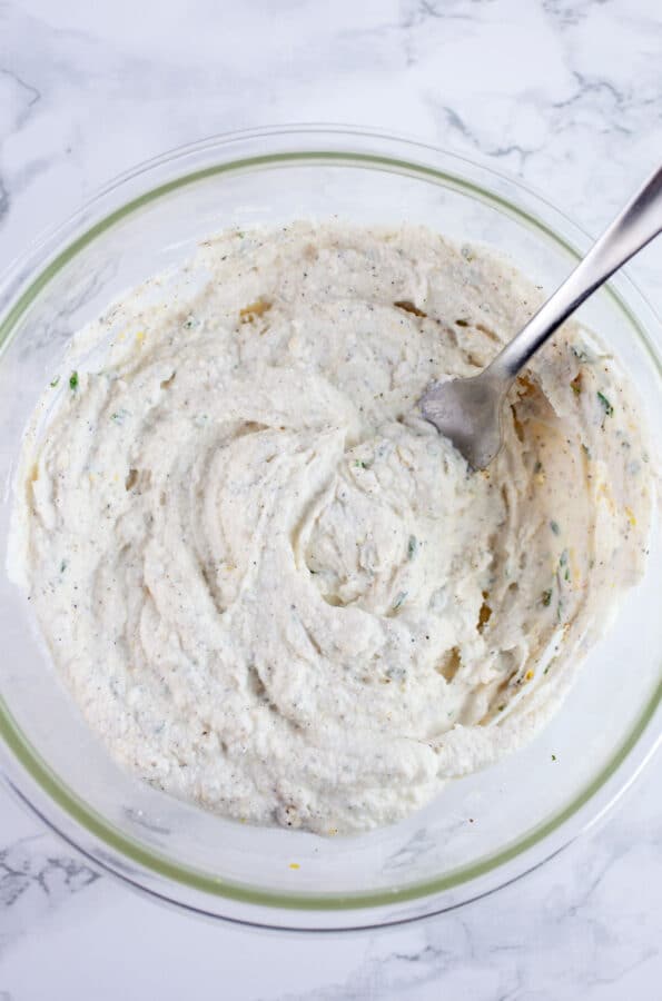 Lemon herb ricotta cheese mixture in small glass bowl with fork.