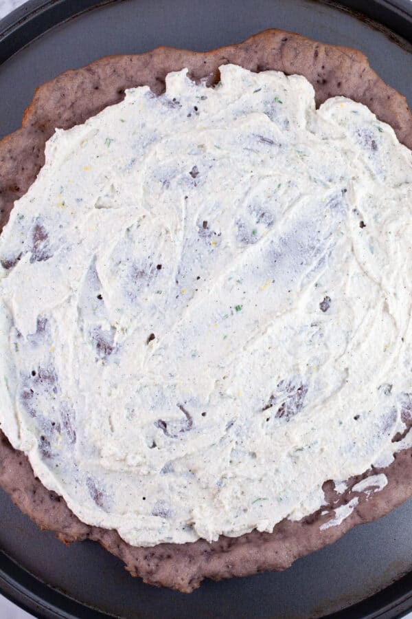 Ricotta spread on par-baked gluten free pizza crust on pizza pan.