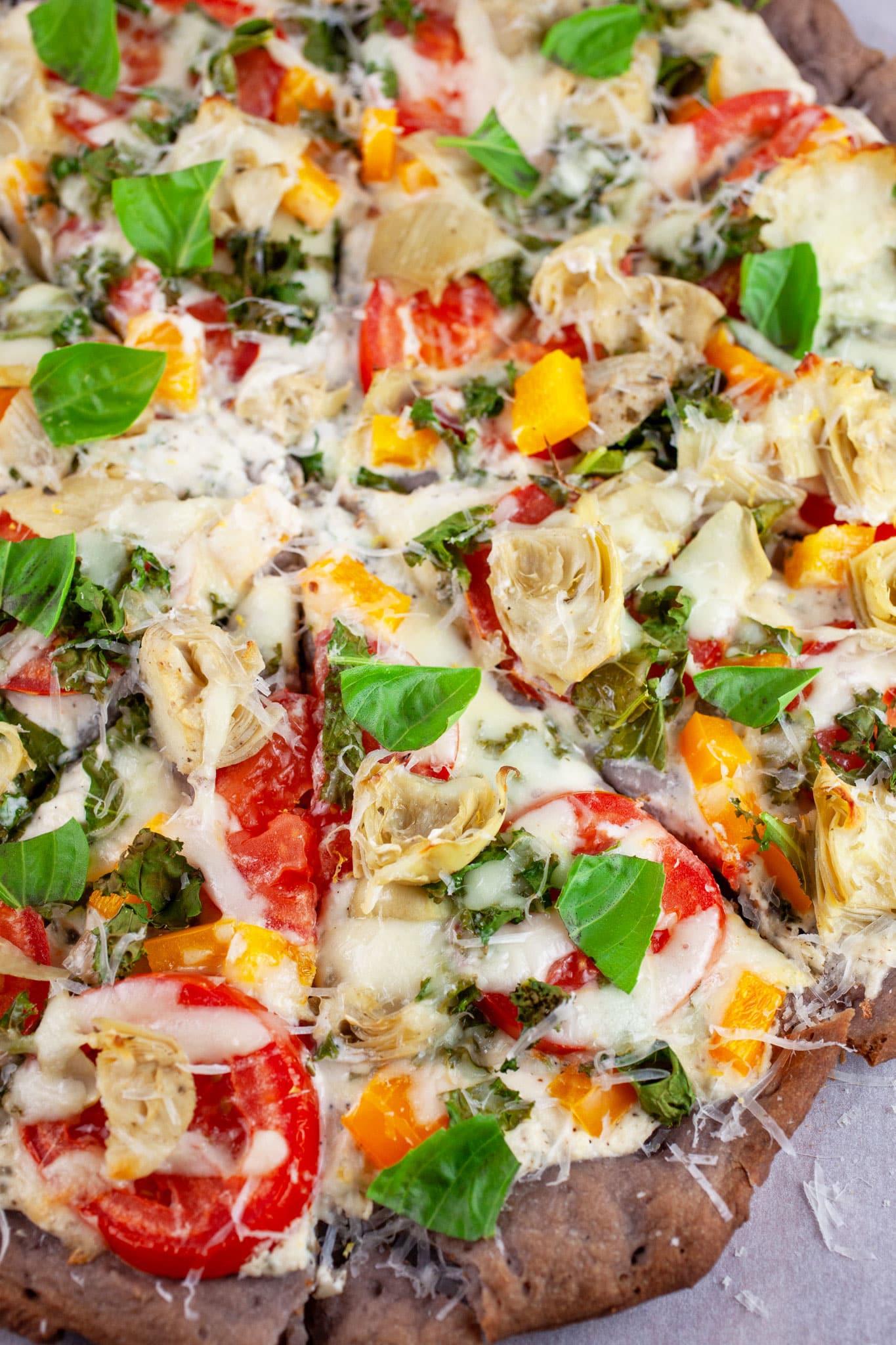 Sliced Farmers Market Pizza garnished with fresh basil and Parmesan cheese.