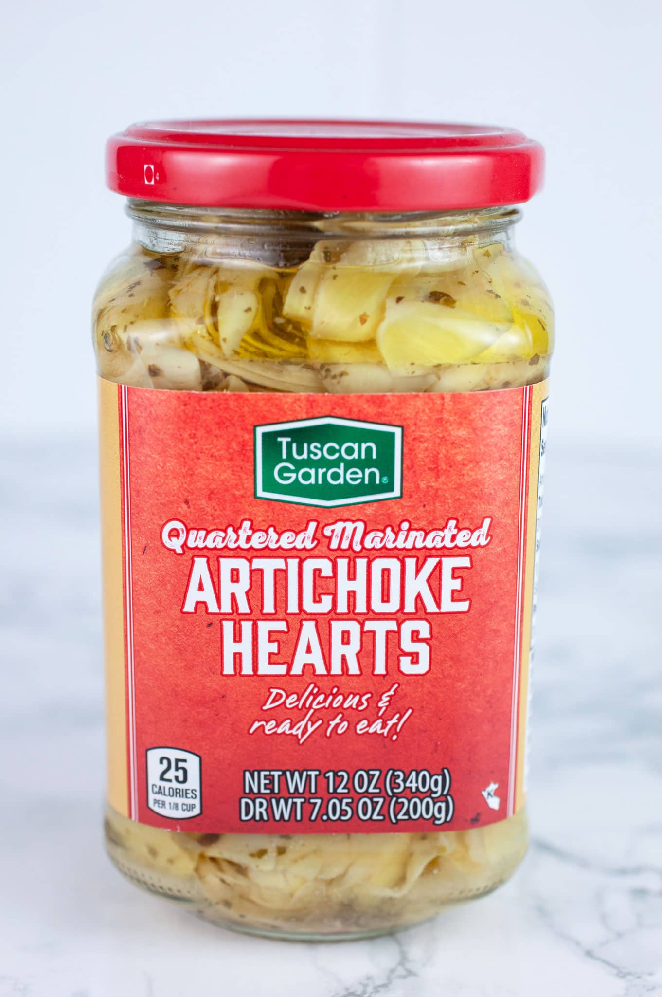 Unopened jar of marinated artichoke hearts on white surface.