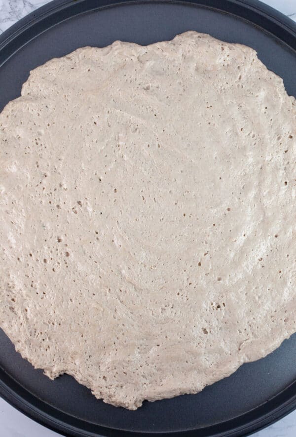 Gluten free pizza dough pressed onto pizza pan.
