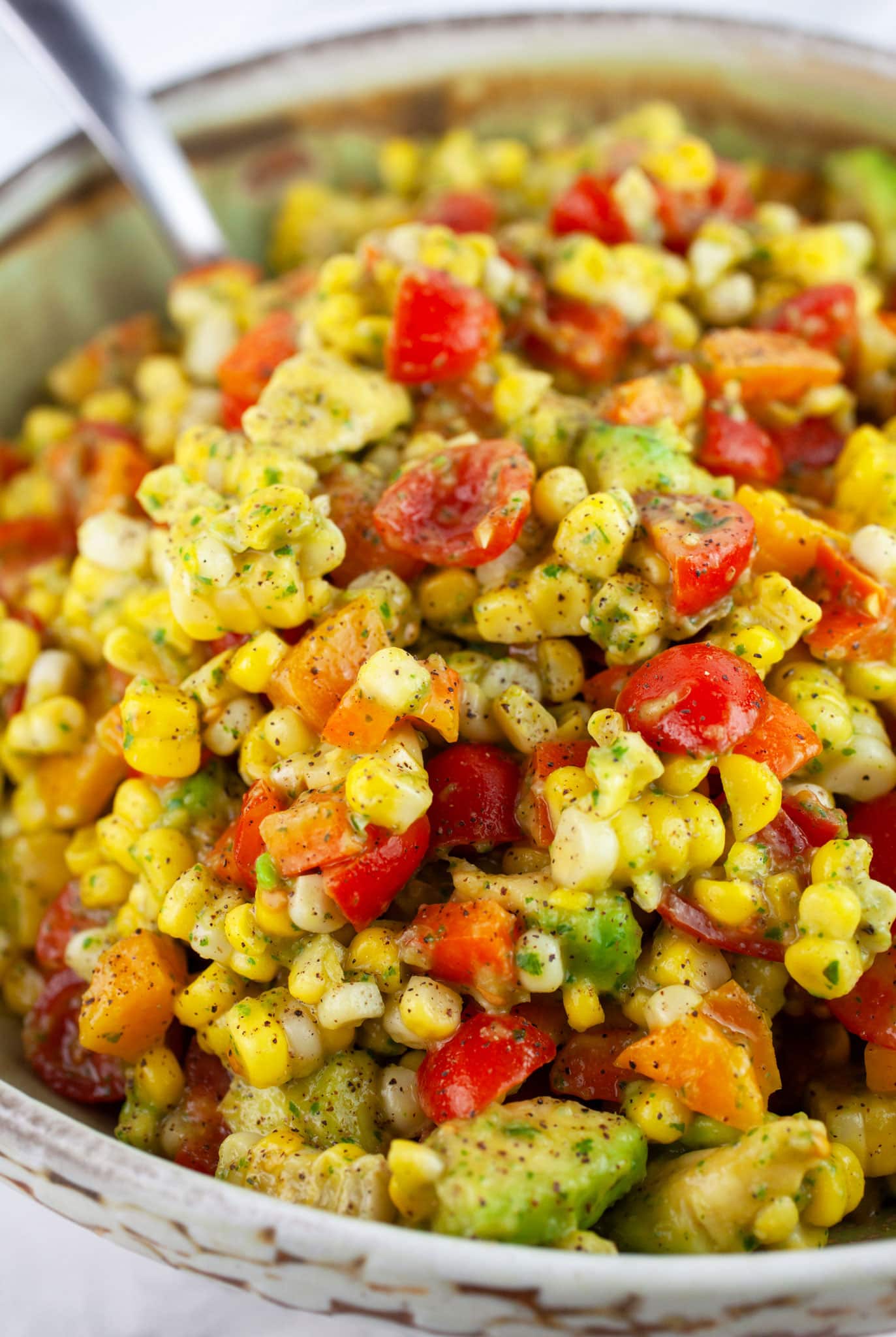 Tomato corn salad with basil vinaigrette in ceramic bowl with metal spoon.
