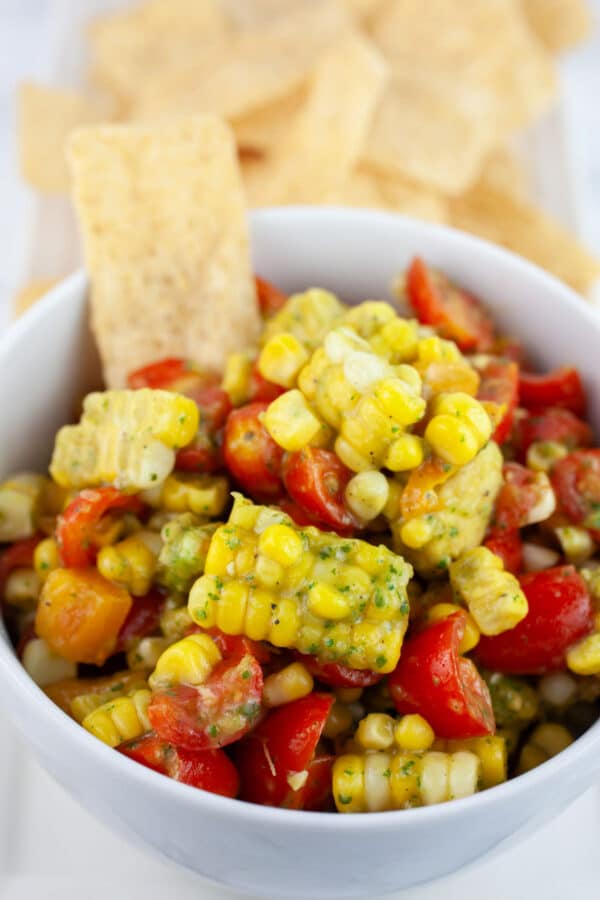 Corn tomato salad in small white bowl with tortilla chips.
