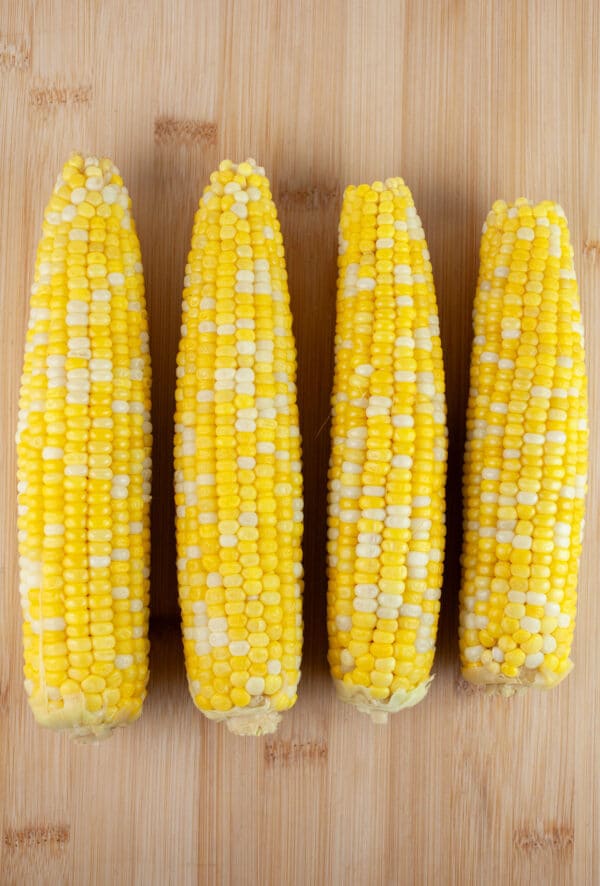 Cooked cobs of sweet corn on wooden cutting board.