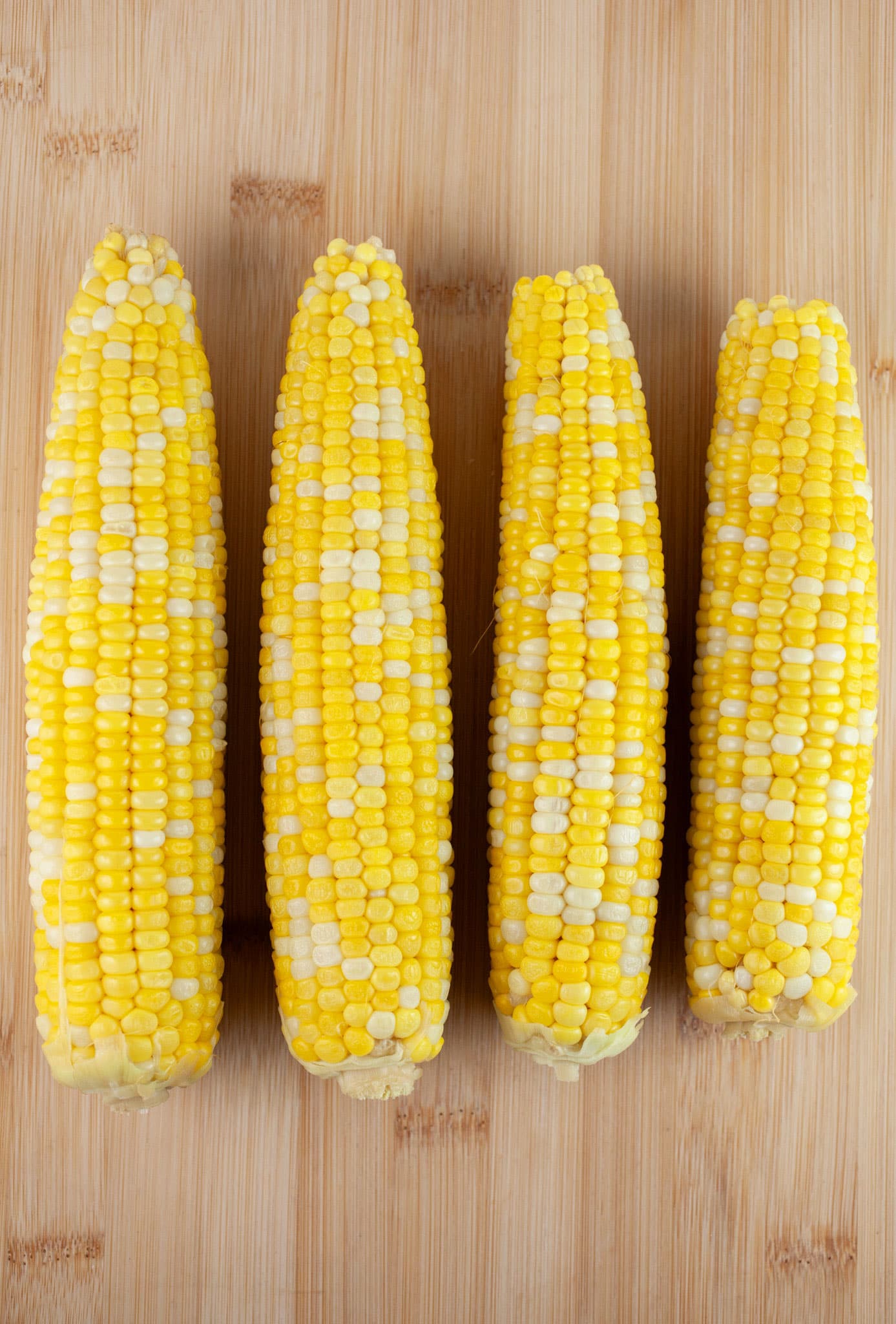 Cooked cobs of sweet corn on wooden cutting board.