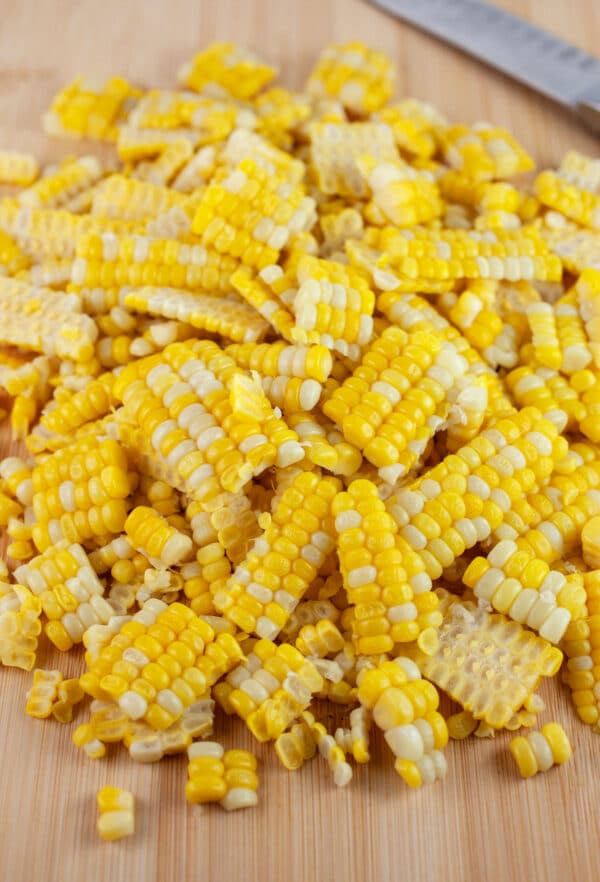 Sweet corn cut from the cob on wooden cutting board with knife.