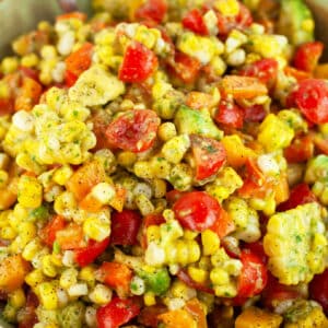 Tomato corn avocado salad in ceramic bowl with spoon.