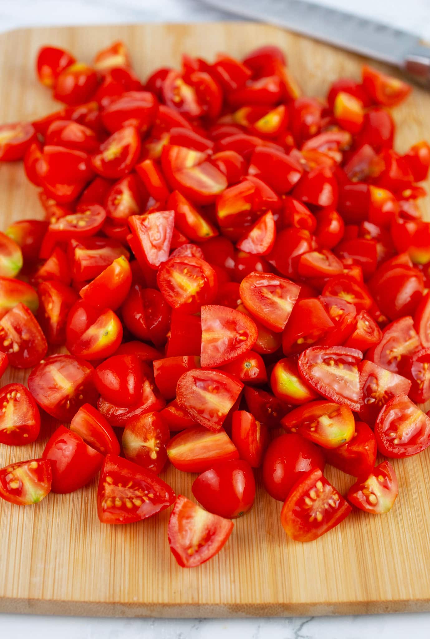 Diced grape tomatoes on wooden cutting board with knife.