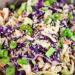 Asian cabbage slaw in ceramic bowl garnished with green onions and sesame seeds.