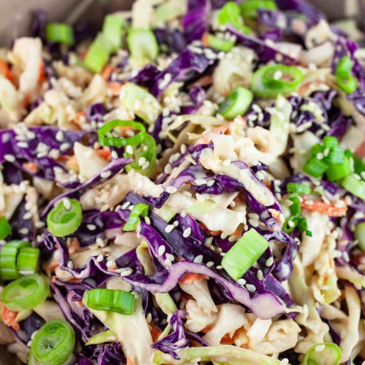 Asian cabbage slaw in ceramic bowl garnished with green onions and sesame seeds.