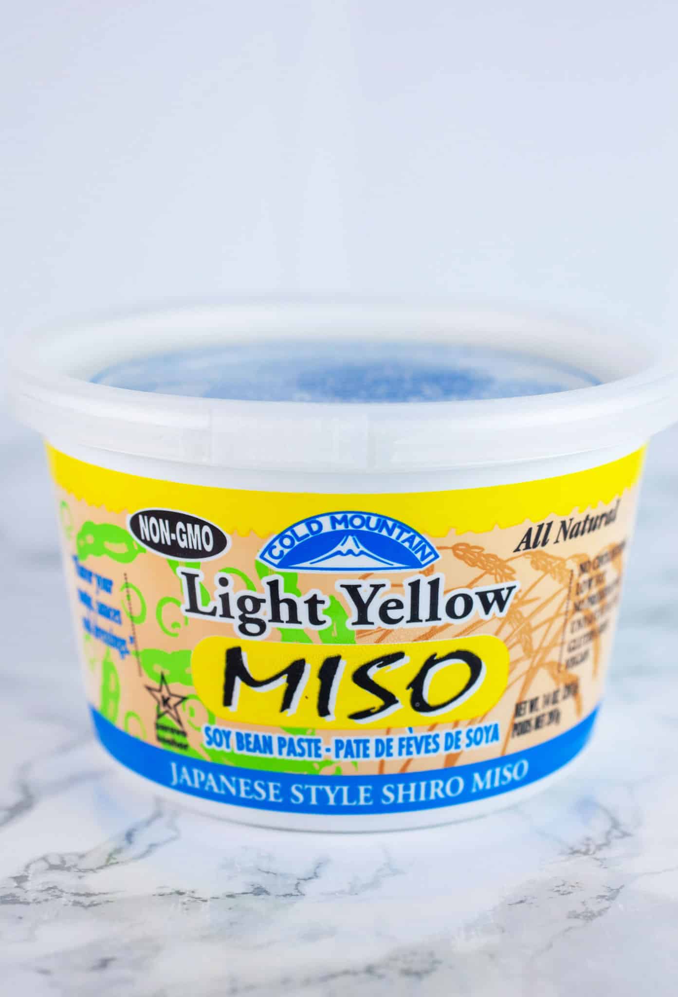 Unopened container of yellow miso on white surface.