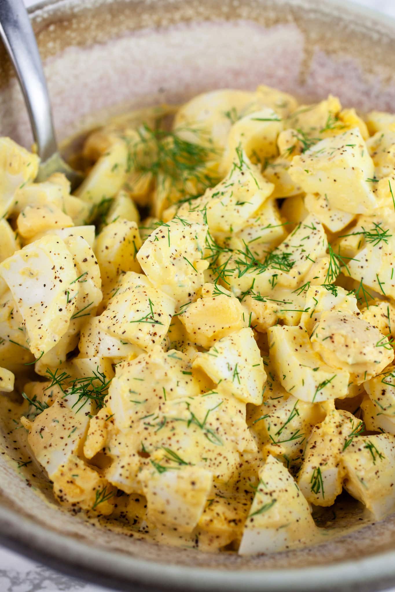 Lemon dill egg salad in ceramic bowl with spoon.