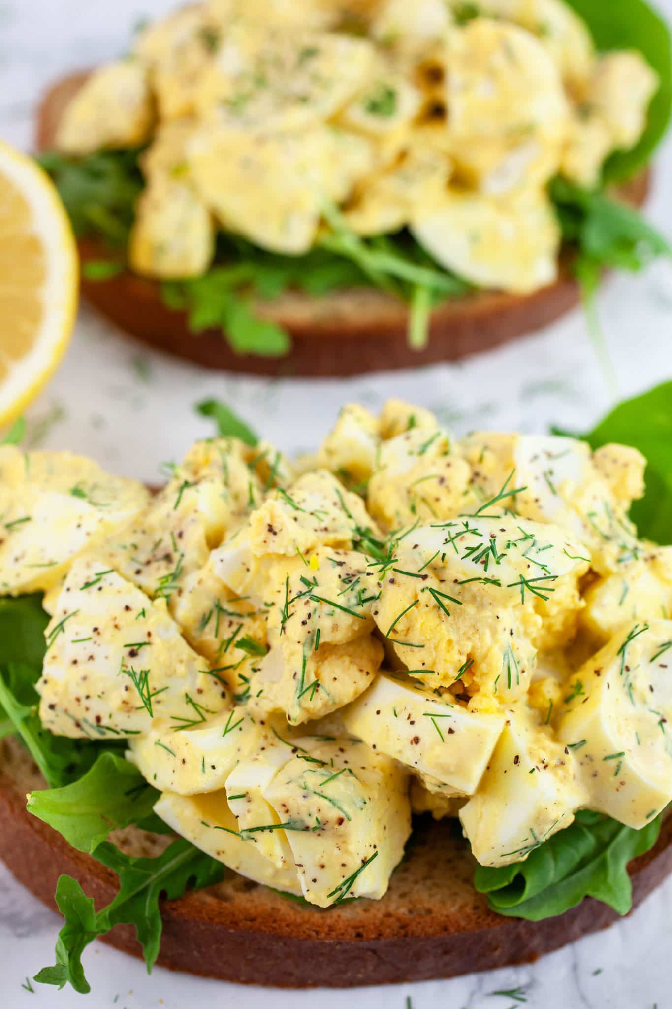 Open-faced egg salad sandwiches with arugula garnished with fresh dill.