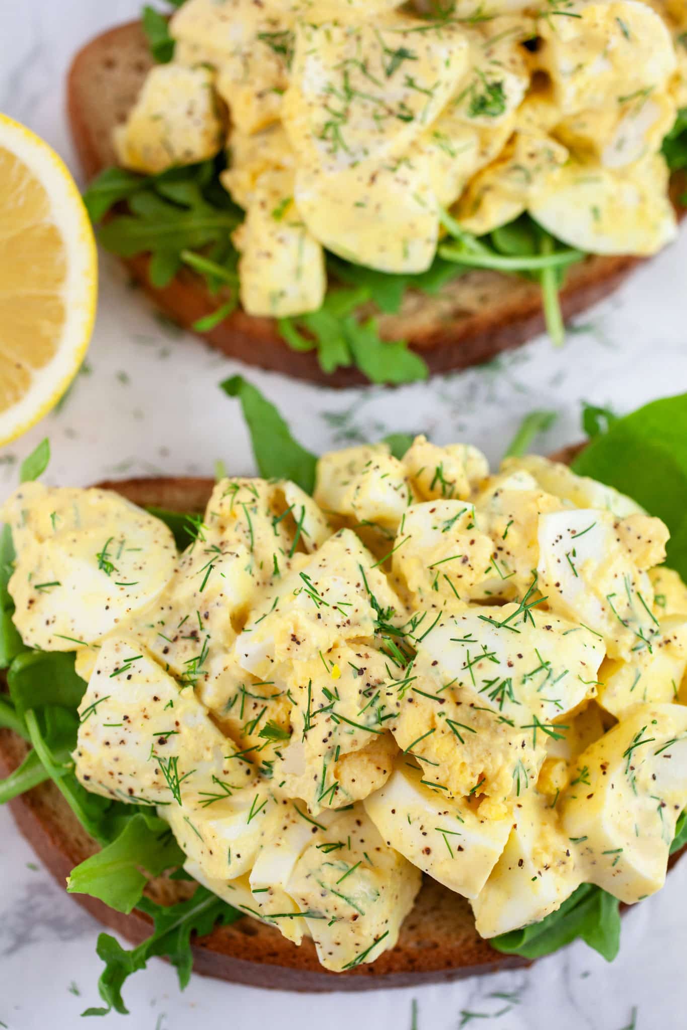 Open faced dill egg salad sandwiches with arugula garnished with fresh dill.