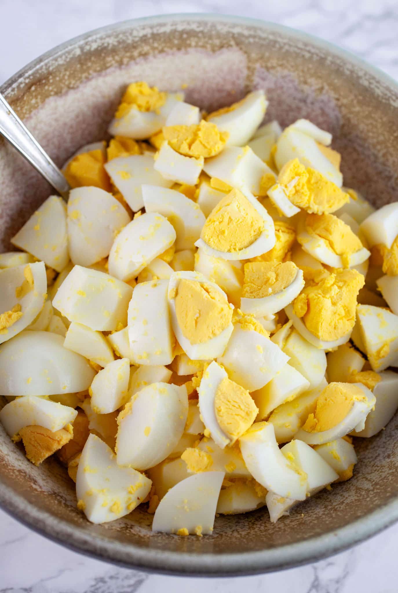 Chopped hard boiled eggs in ceramic bowl with spoon.