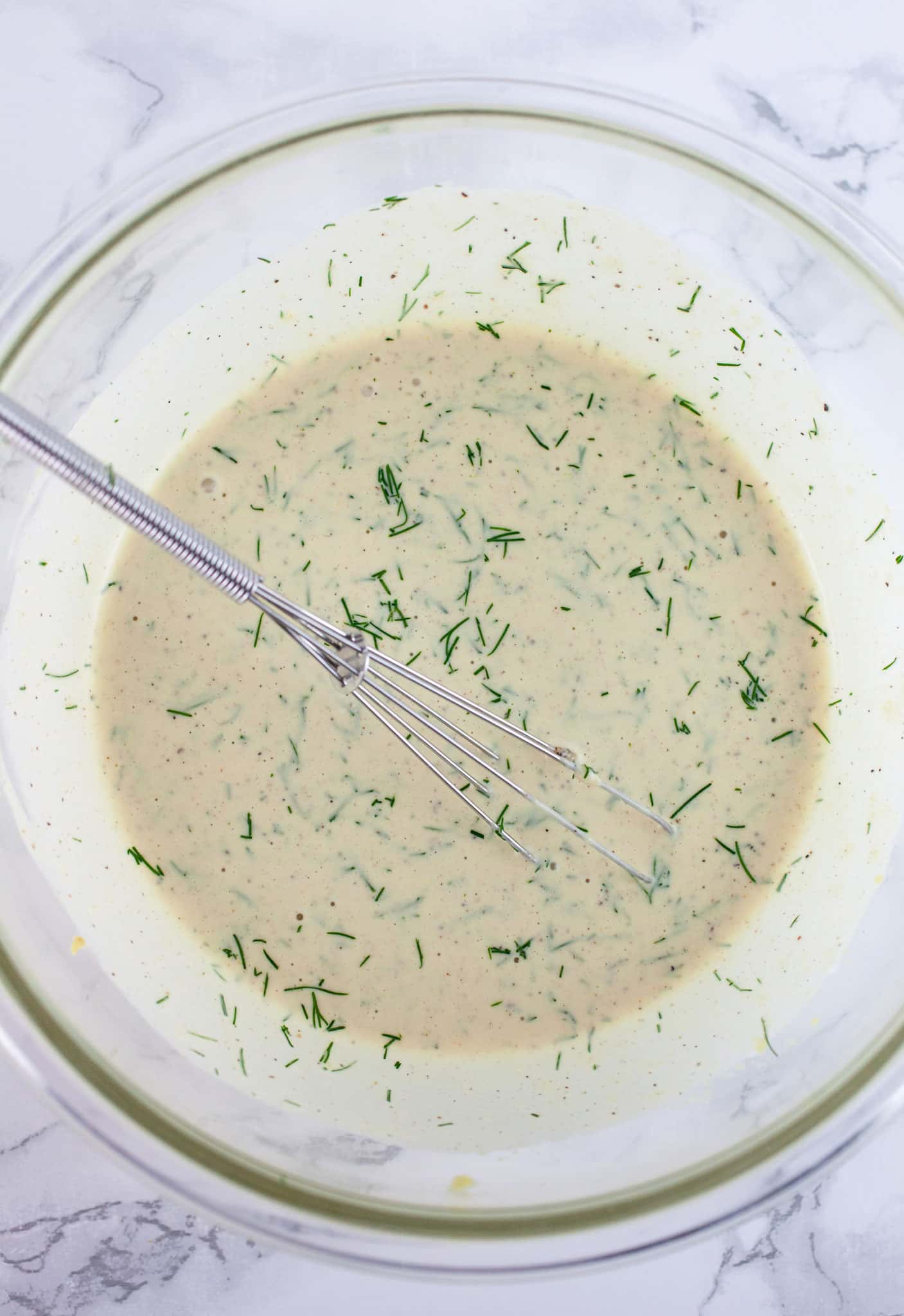Lemon dill dressing in glass bowl with small whisk.