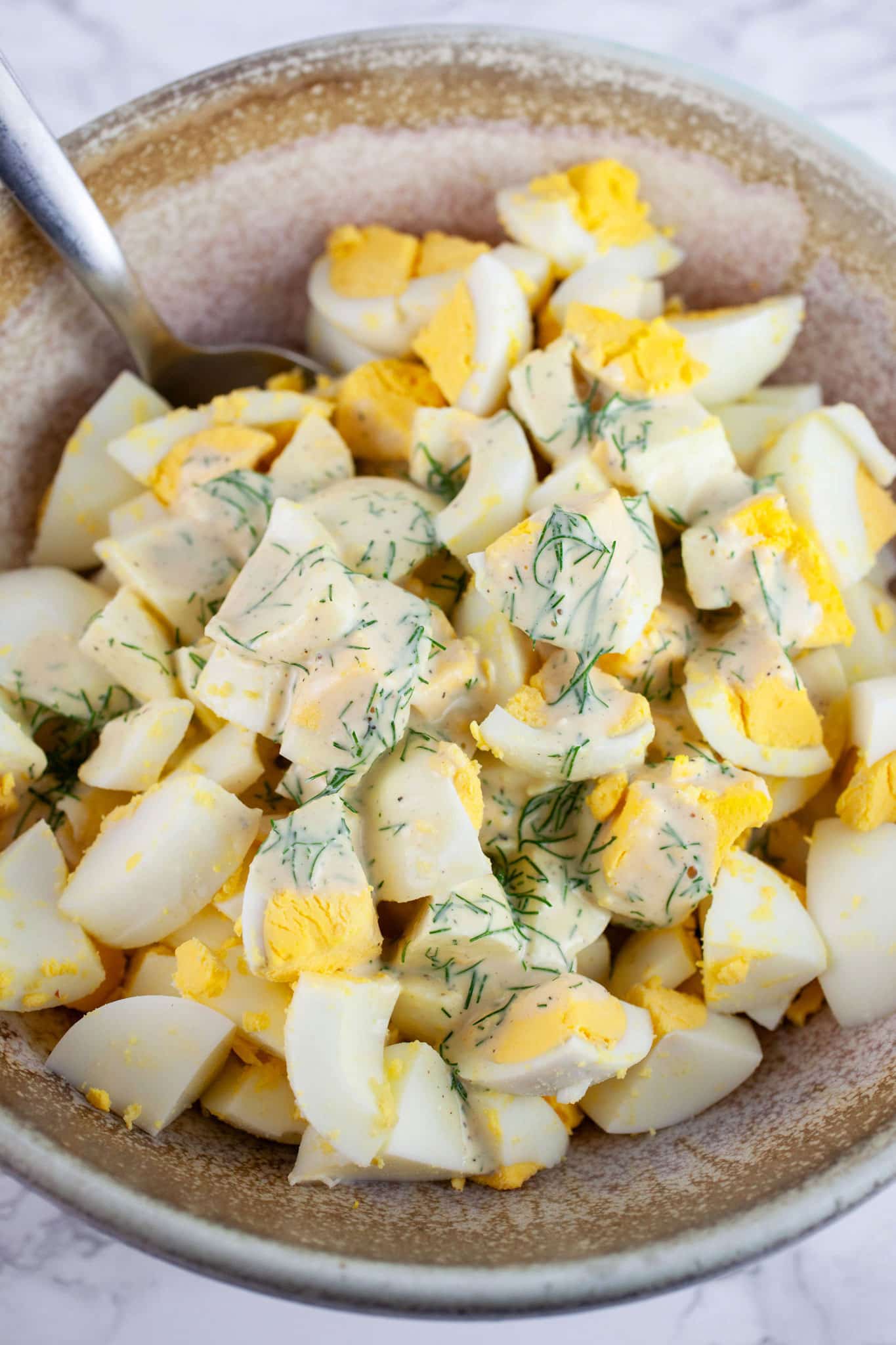 Lemon dill dressing poured on chopped hard boiled eggs in ceramic bowl with spoon.