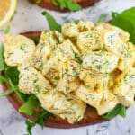 Open faced egg salad sandwich with arugula garnished with fresh dill.