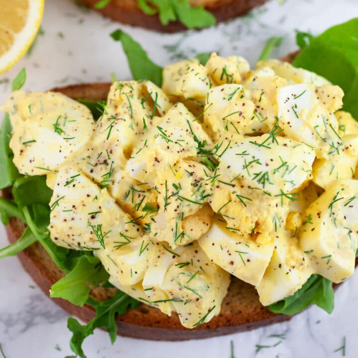 Open faced egg salad sandwich with arugula garnished with fresh dill.