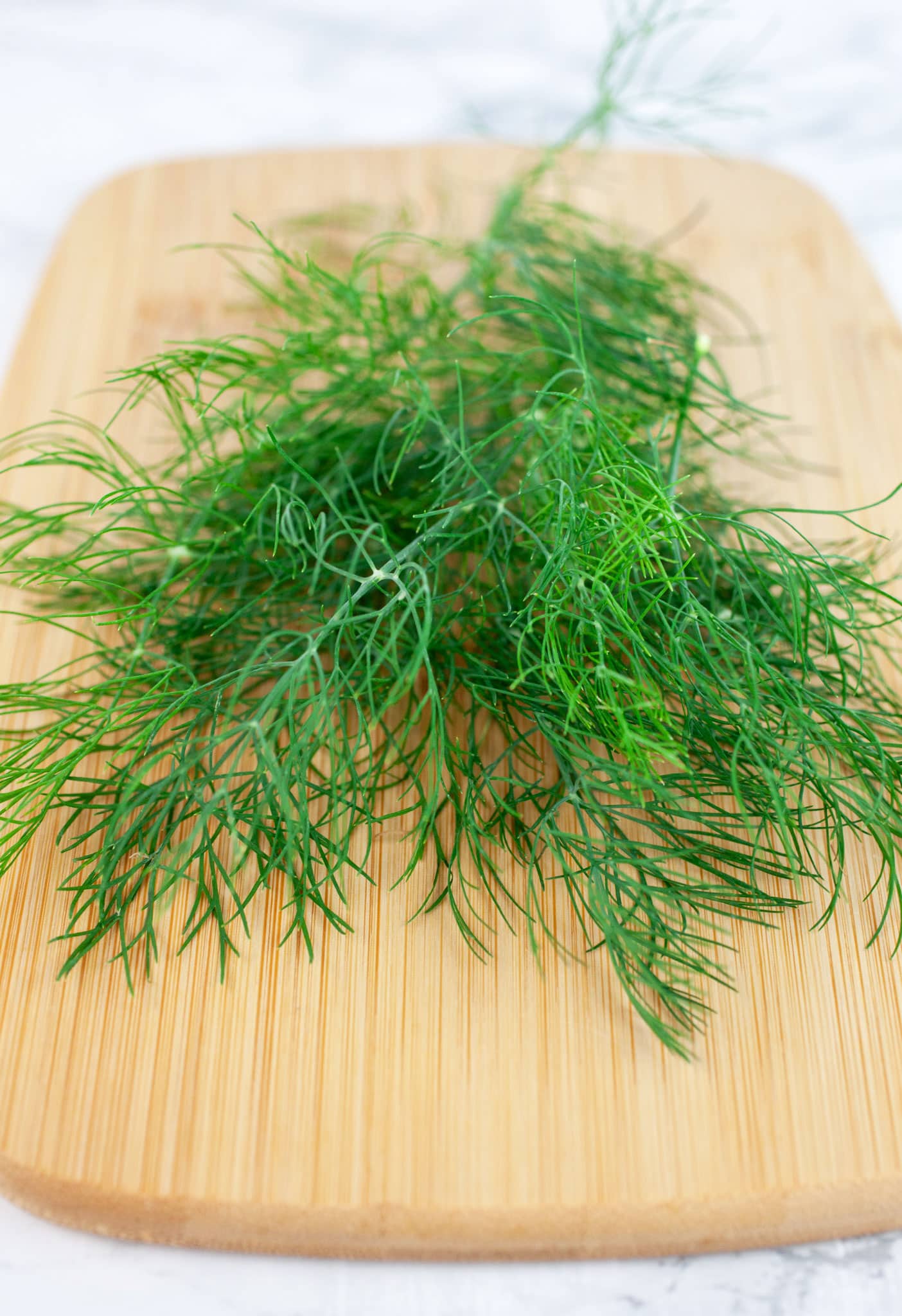 Fresh dill fronds on wooden cutting board.