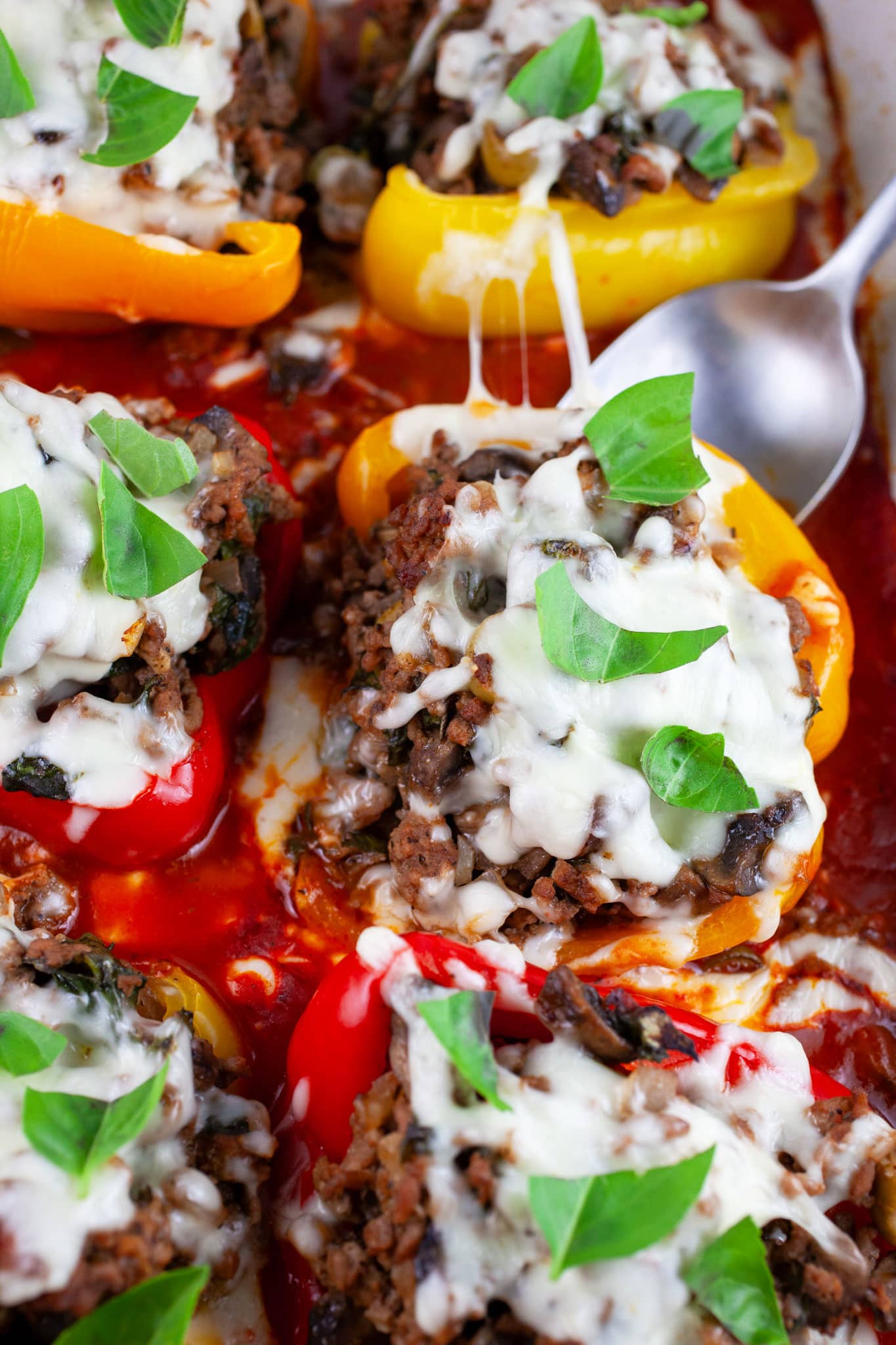 Baked pizza stuffed peppers in casserole dish with spoon garnished with fresh basil.