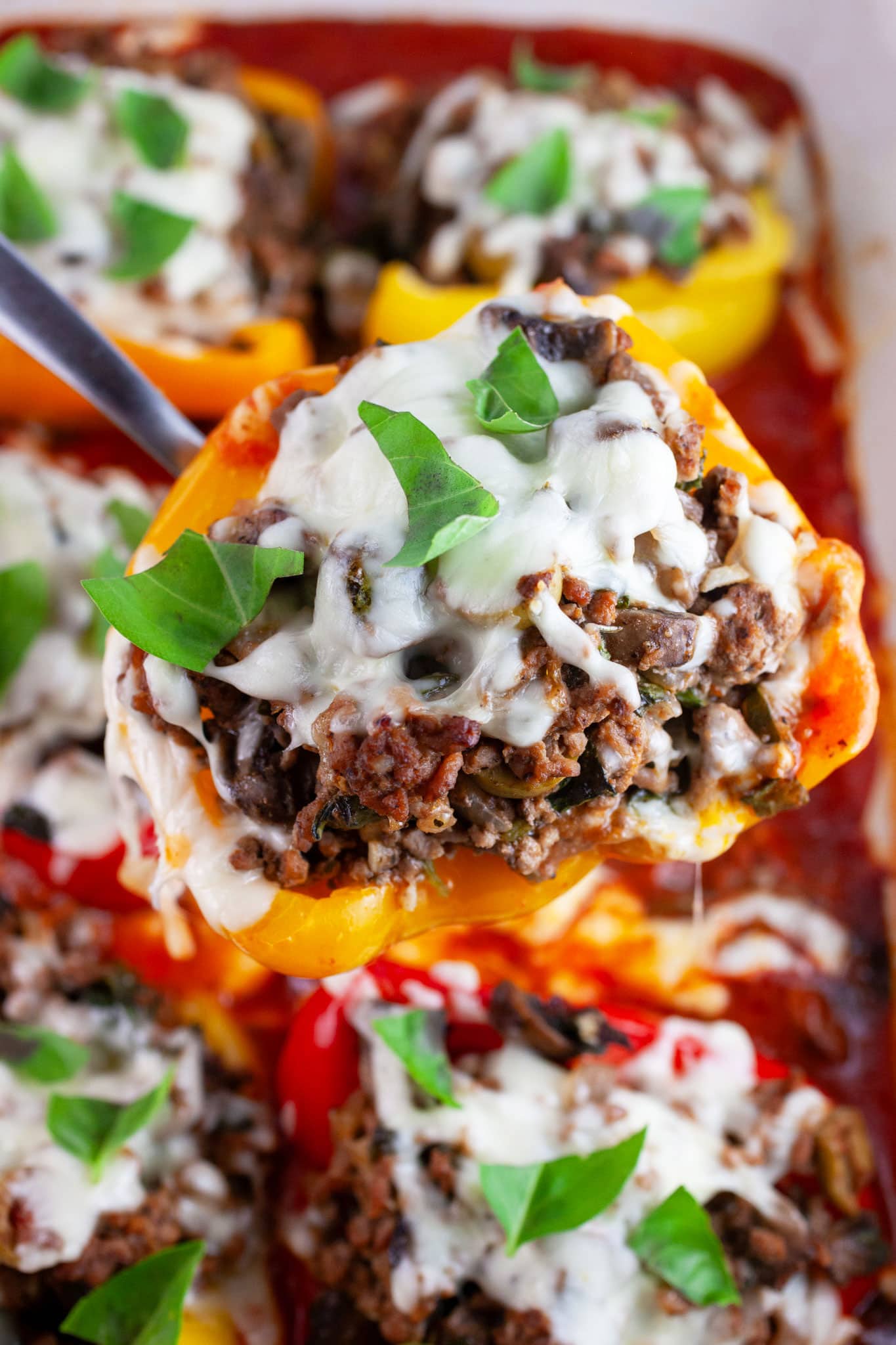 Ground beef stuffed pepper lifted from casserole dish with metal spoon.