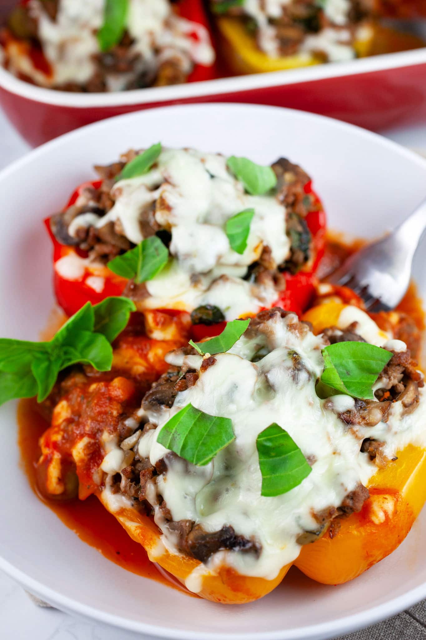 Stuffed bell peppers in white bowl with fork garnished with fresh basil.