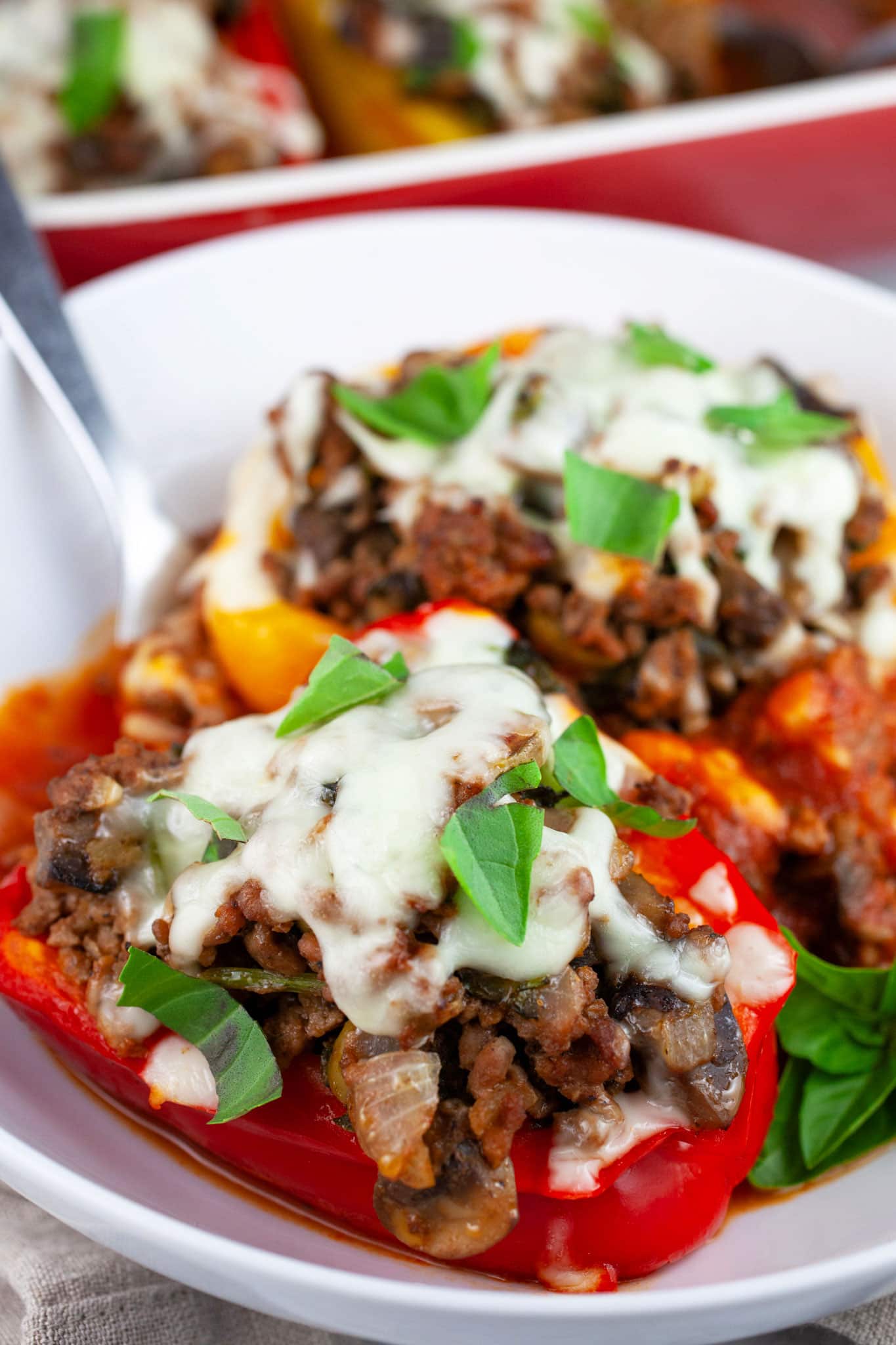 Pizza stuffed bell peppers in white bowl with fork garnished with fresh basil.