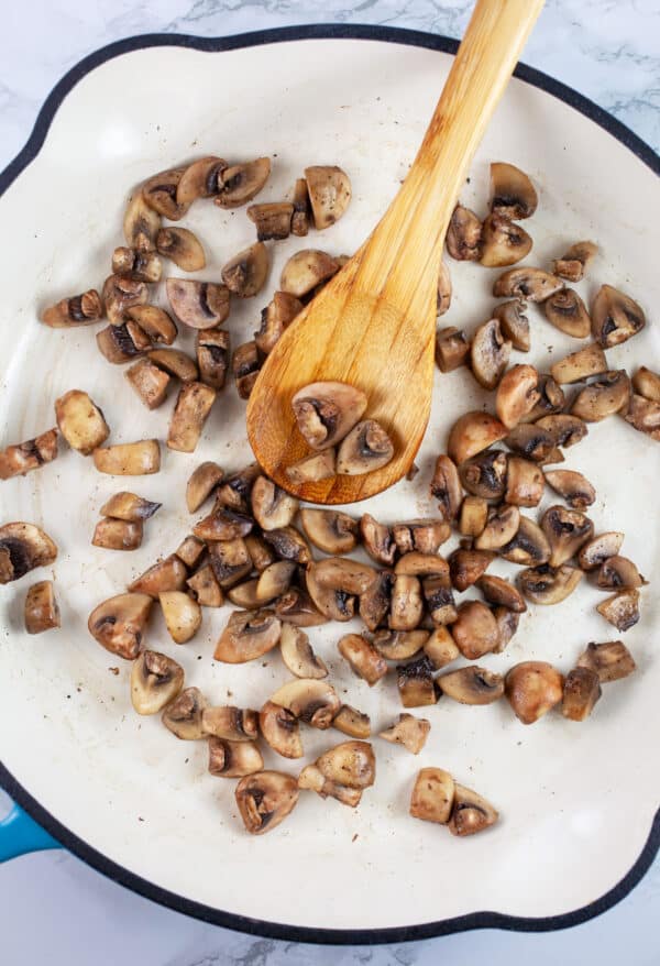 Diced mushrooms sauteed in skillet with wooden spoon.