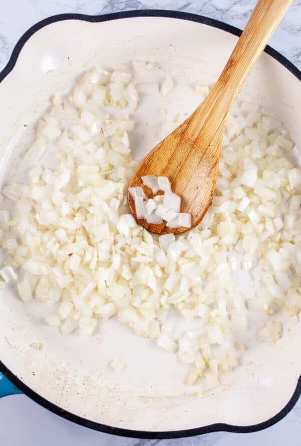 Minced garlic and onions sauteed in skillet with wooden spoon.