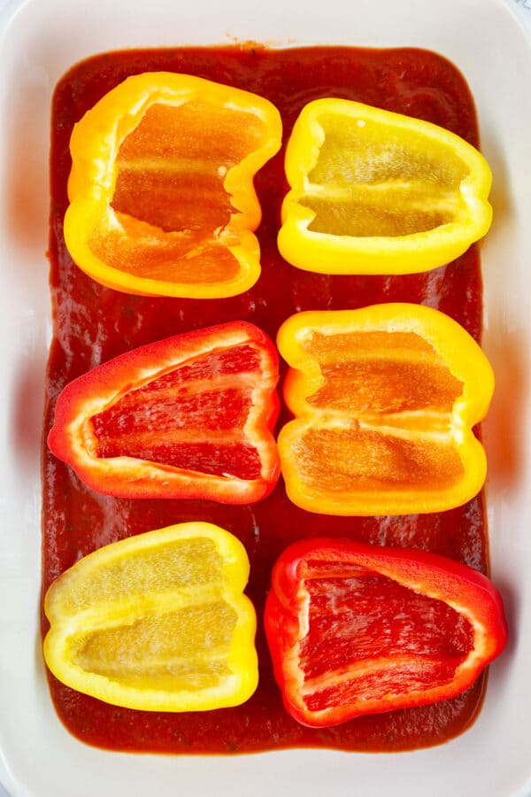 Halved bell peppers in ceramic casserole dish with pizza sauce.