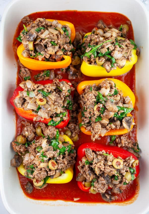 Uncooked bell pepper halves in ceramic casserole dish with pizza sauce.