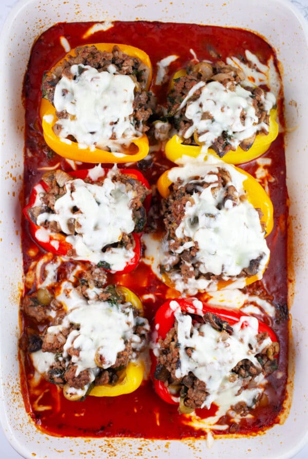 Cooked stuffed peppers with cheese in ceramic casserole dish with pizza sauce.