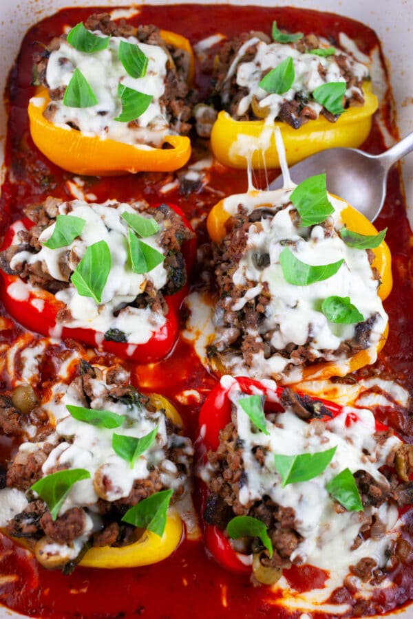 Pizza stuffed peppers in ceramic casserole dish with spoon garnished with fresh basil.