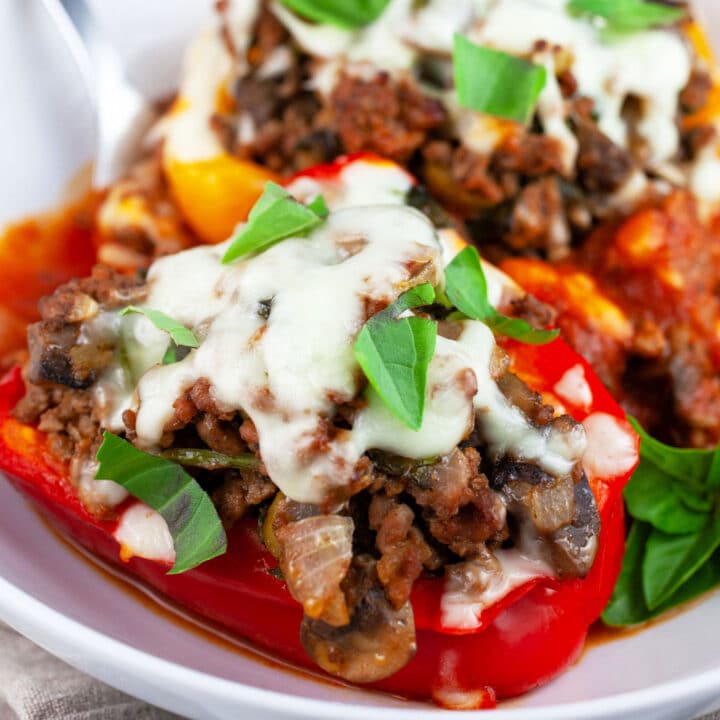 Pizza stuffed peppers in white bowl with fork garnished with fresh basil.