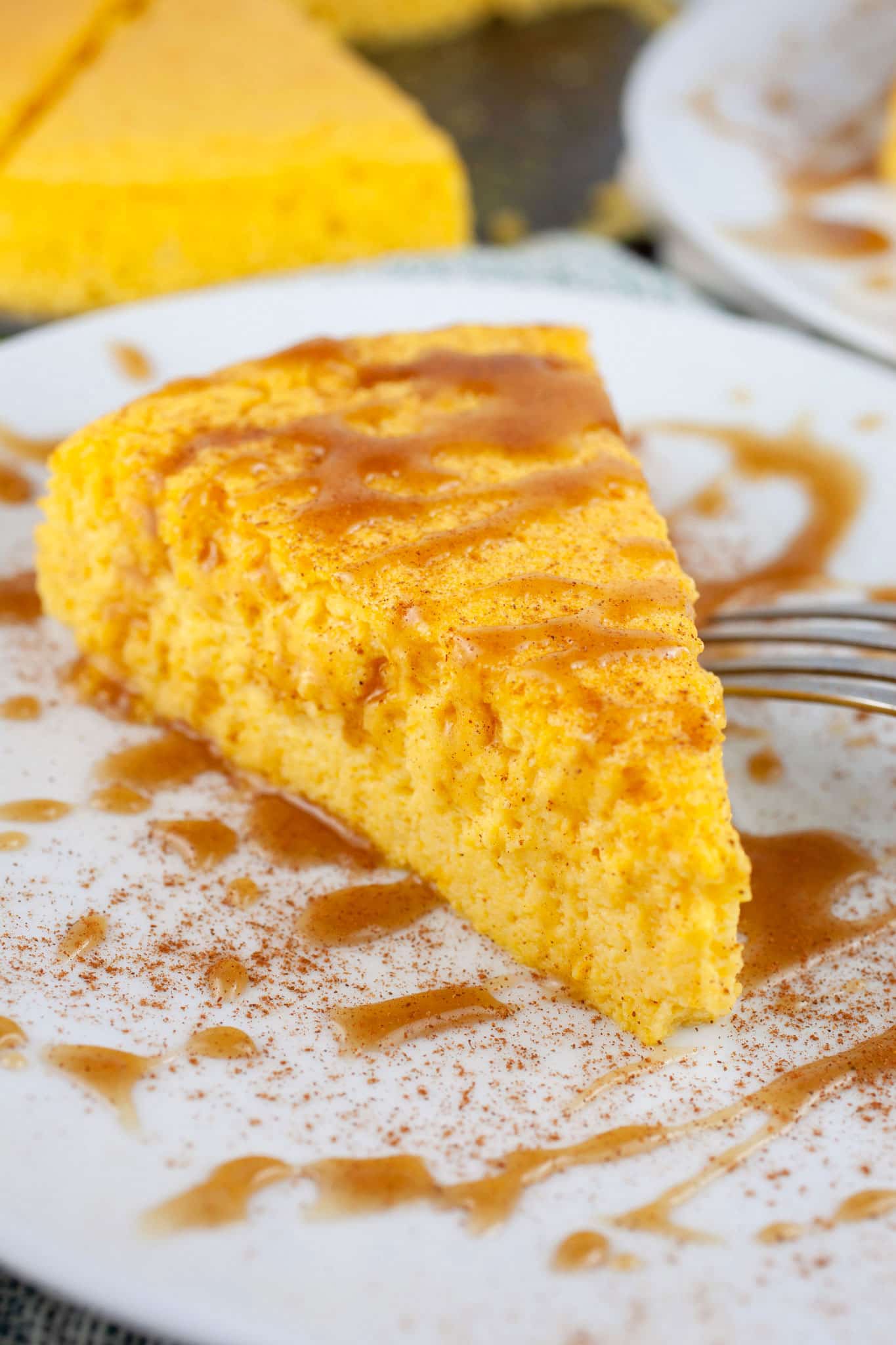Slice of crustless pumpkin cheesecake with caramel sauce on white plate with fork.