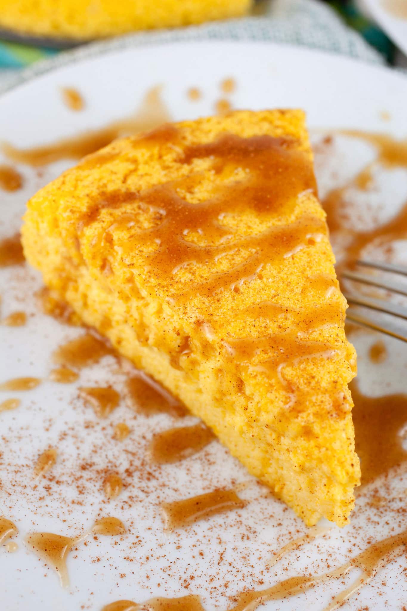 Slice of crustless pumpkin cheesecake with caramel sauce on white plate with fork.