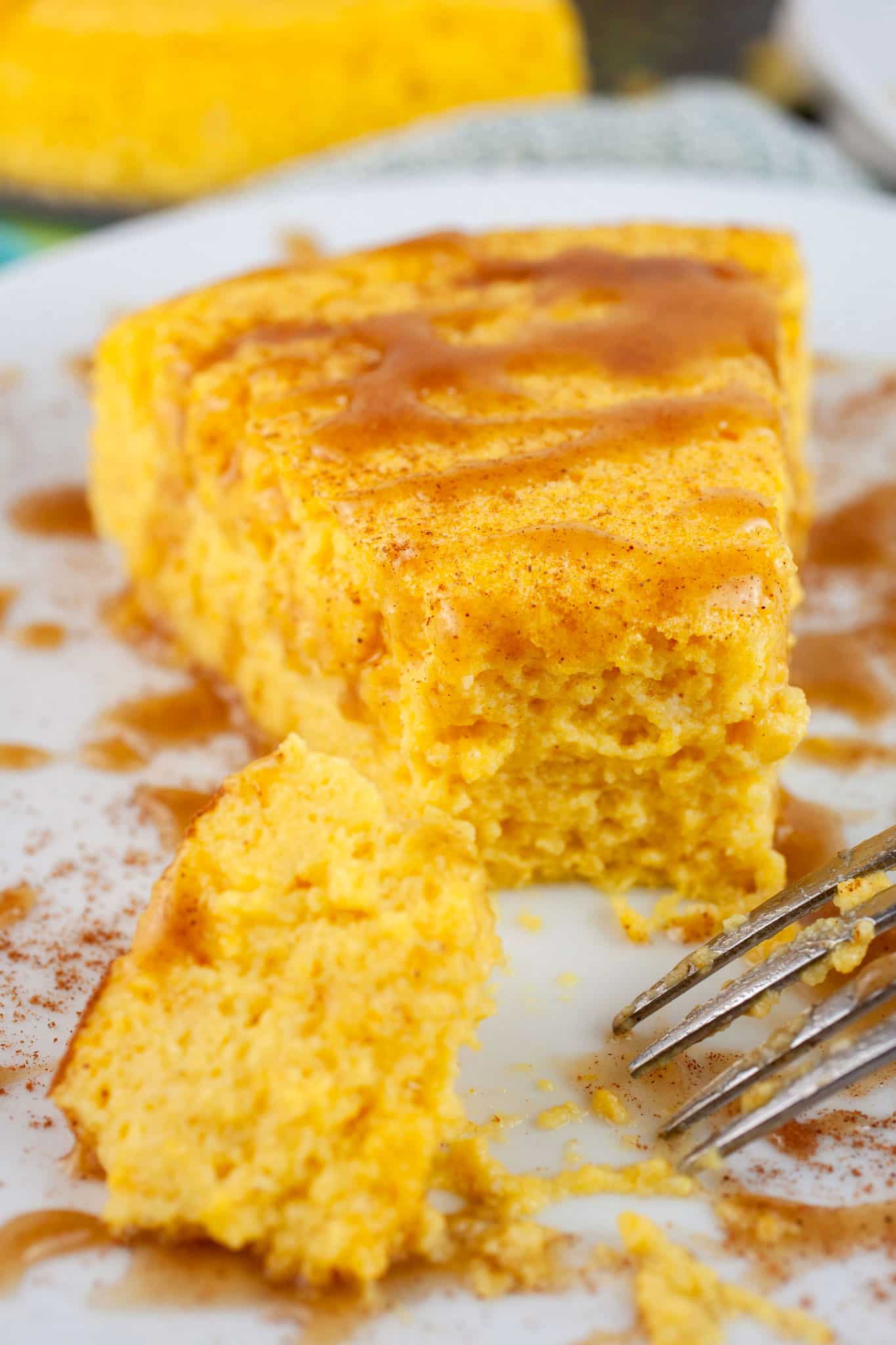 Slice of crustless pumpkin cheesecake with caramel sauce cut with fork on white plate.