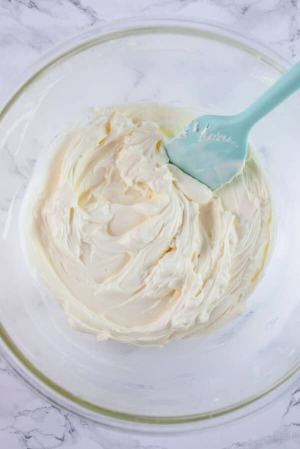 Cream cheese mixture in glass bowl with light blue spatula.