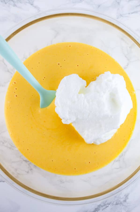 Meringue with pumpkin cheesecake batter in glass bowl with light blue spatula.