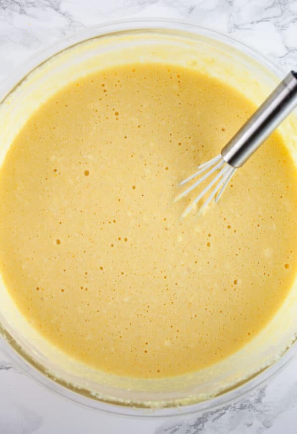 Cheesecake batter in glass bowl with whisk.