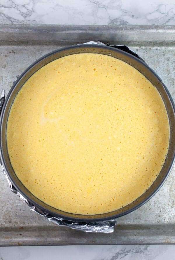 Cheesecake batter in springform pan in rectangular pan full of water.