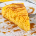 Slice of crustless pumpkin cheesecake with caramel sauce on white plate with fork.