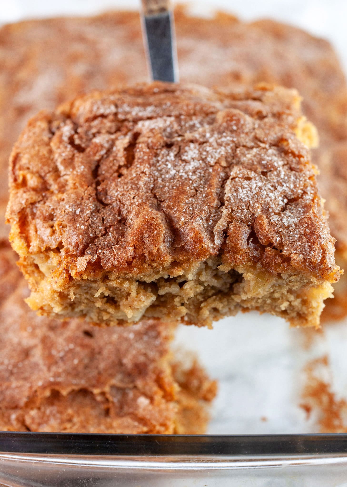Slice of gluten free apple cake lifted from glass baking pan with spatula.