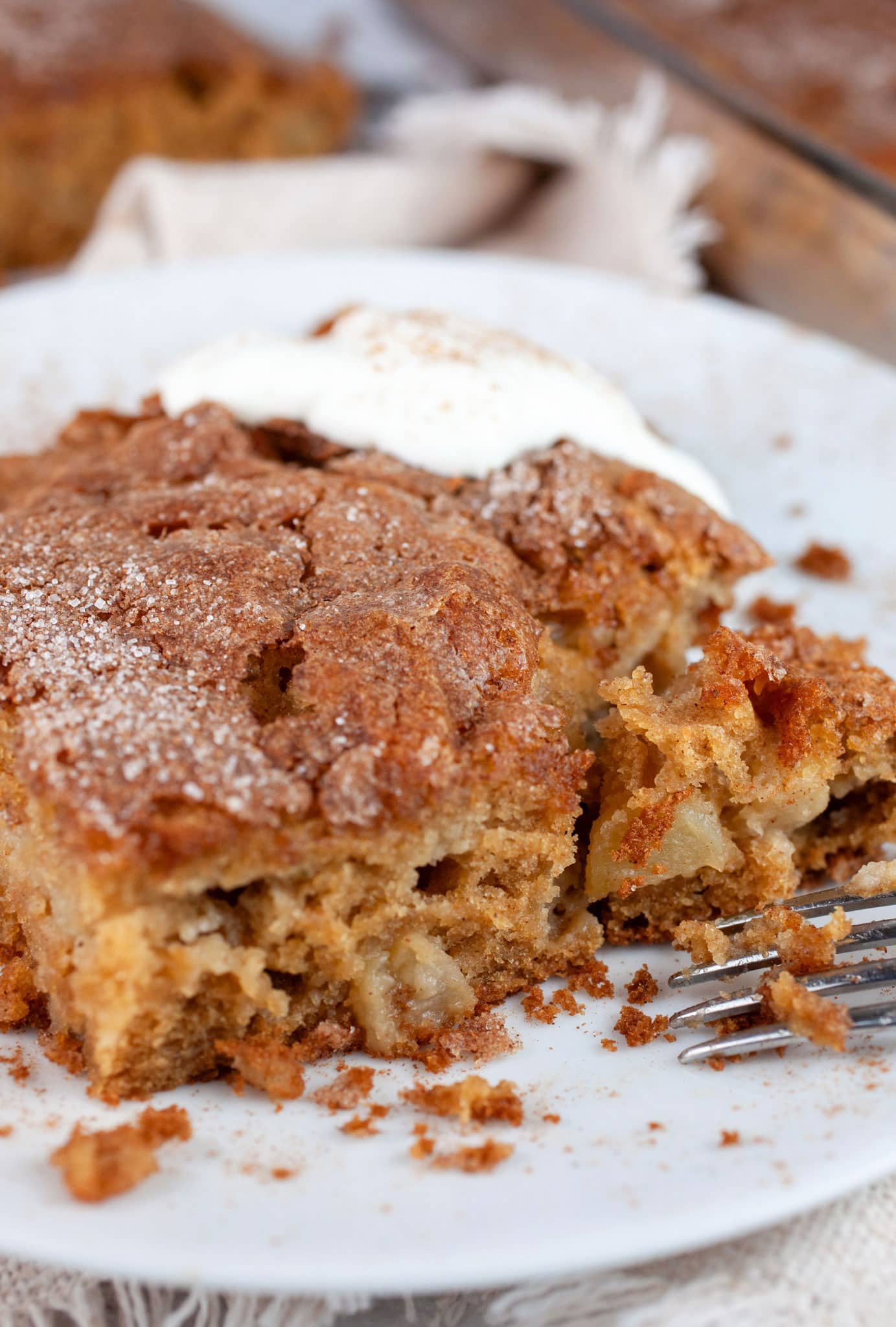 Slice of gluten free apple cake with whipped cream on white plate with fork.