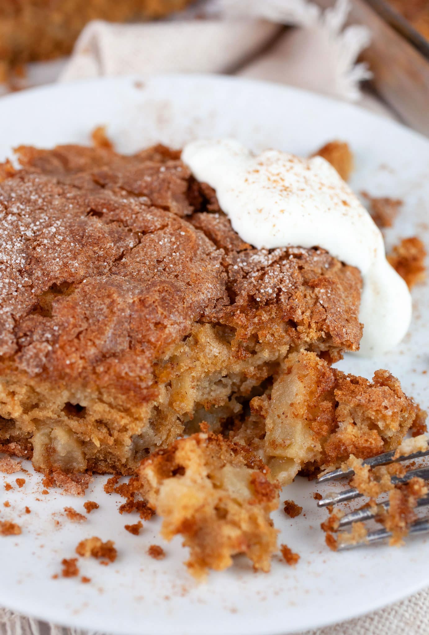 Gluten free apple cake with whipped cream on white plate with fork.