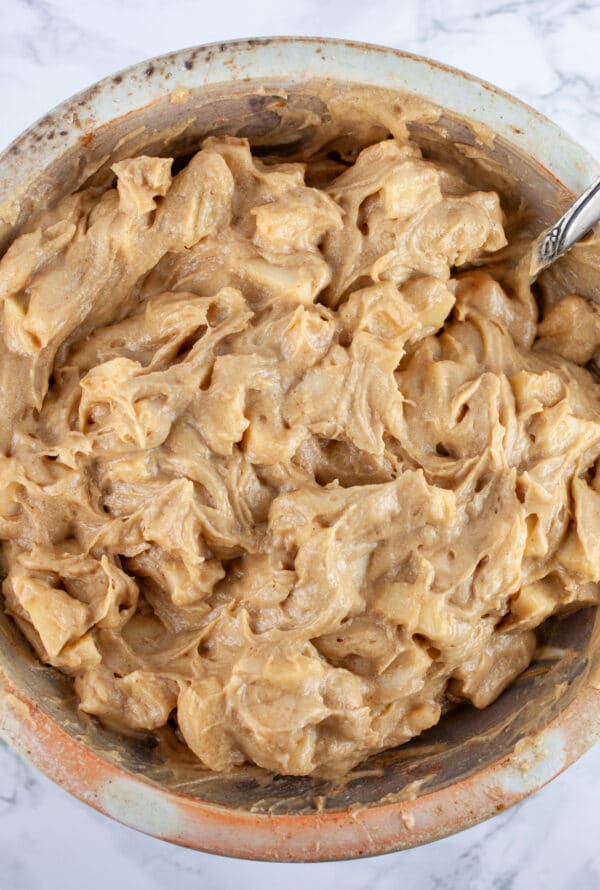 Apples mixed into cake batter in ceramic bowl with spoon.