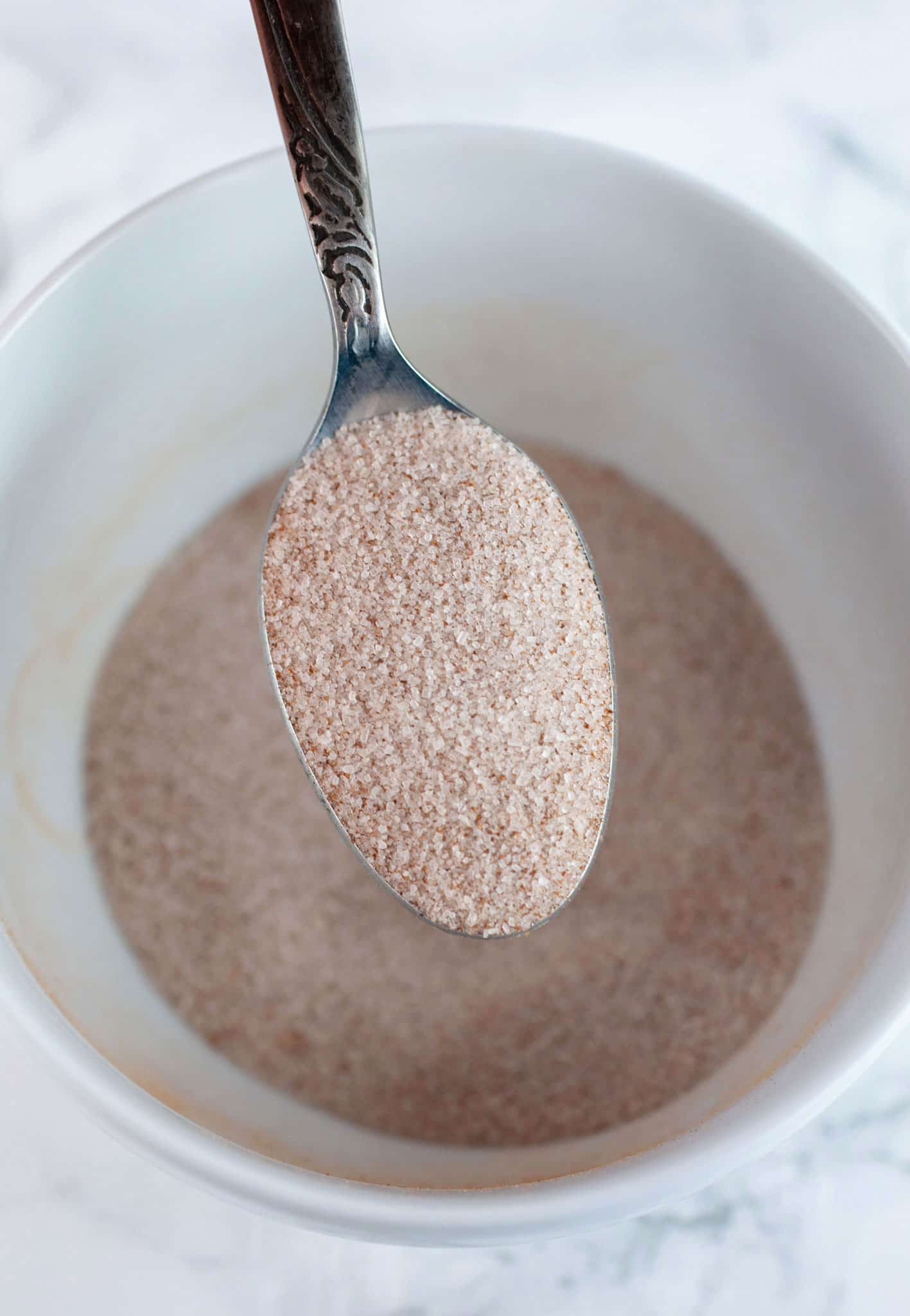 Spoonful of cinnamon sugar mixture lifted from small white bowl.